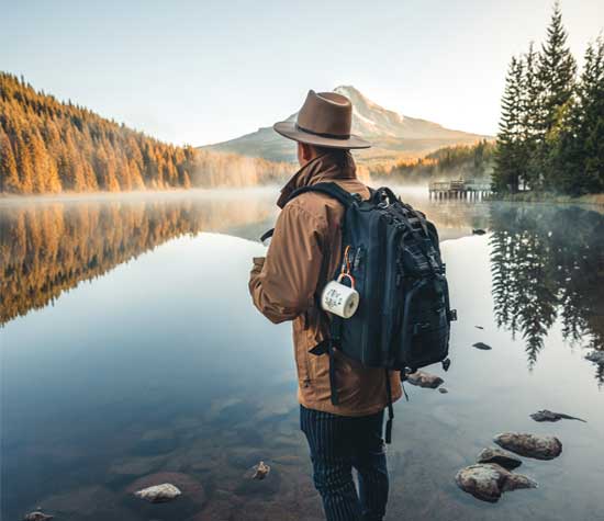 Man standing next to lake wearing a backpack