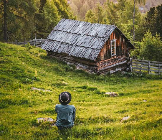 man sitting in front of a cabin in a open field