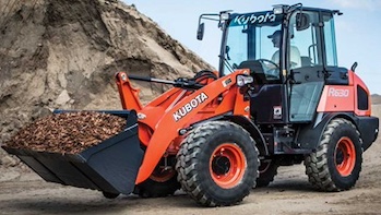 An orange Kubota R530 loader carries a bucket full of dirt or mulch at a construction or landscaping site.