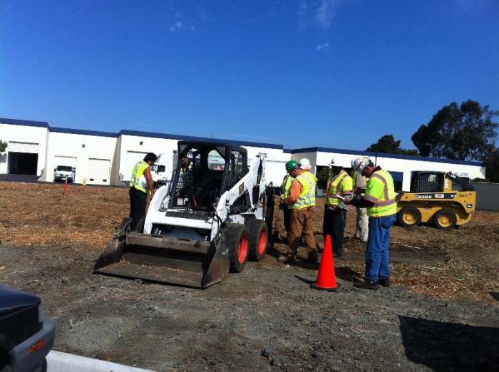 workers standing next to skid steer loader/tractor